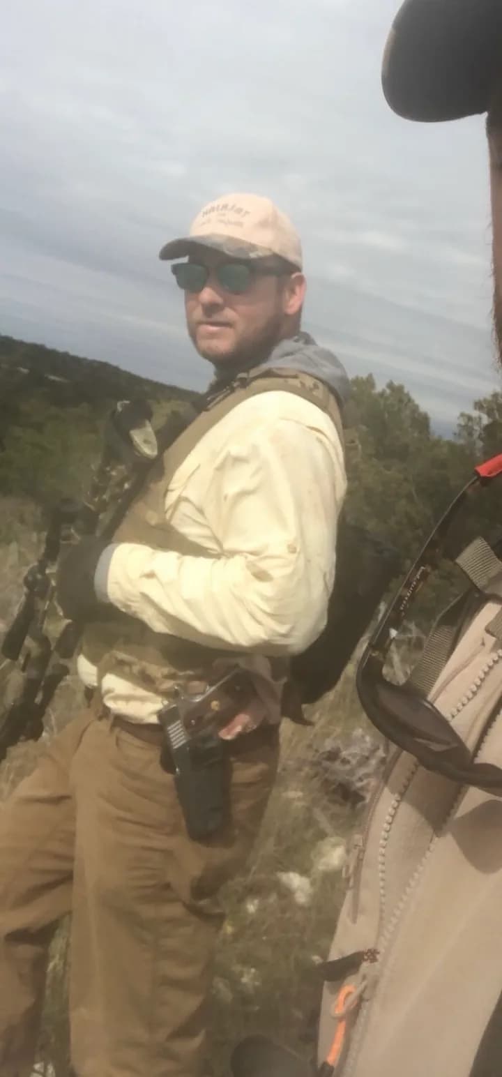 Michael McCammon bowhunting in cedar brush country, carrying a compound bow and a camouflage pack.