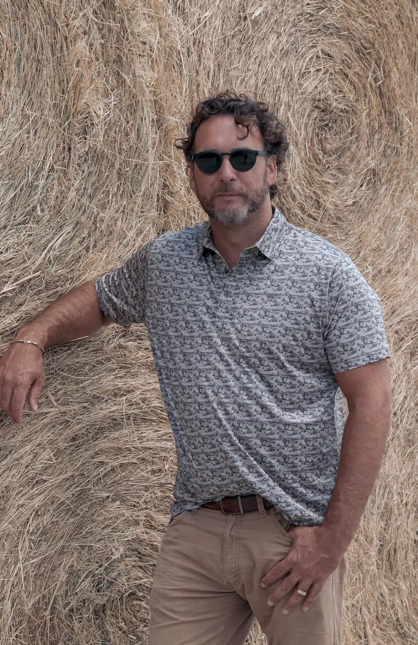 Michael McCammon, founder of Bare Bone Outdoor Services, leaning against a stack of round hay bales.